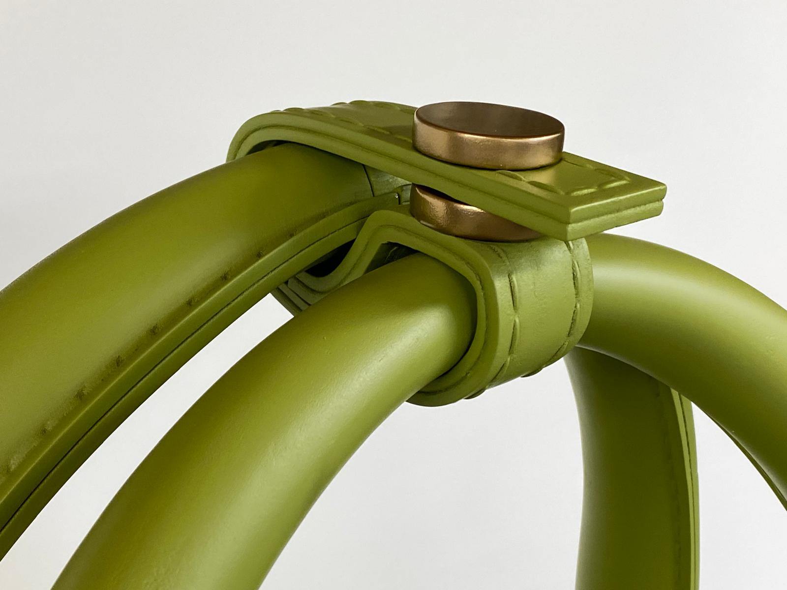 Detalle terminado de las asas, correas y herrajes dorados del bolso verde